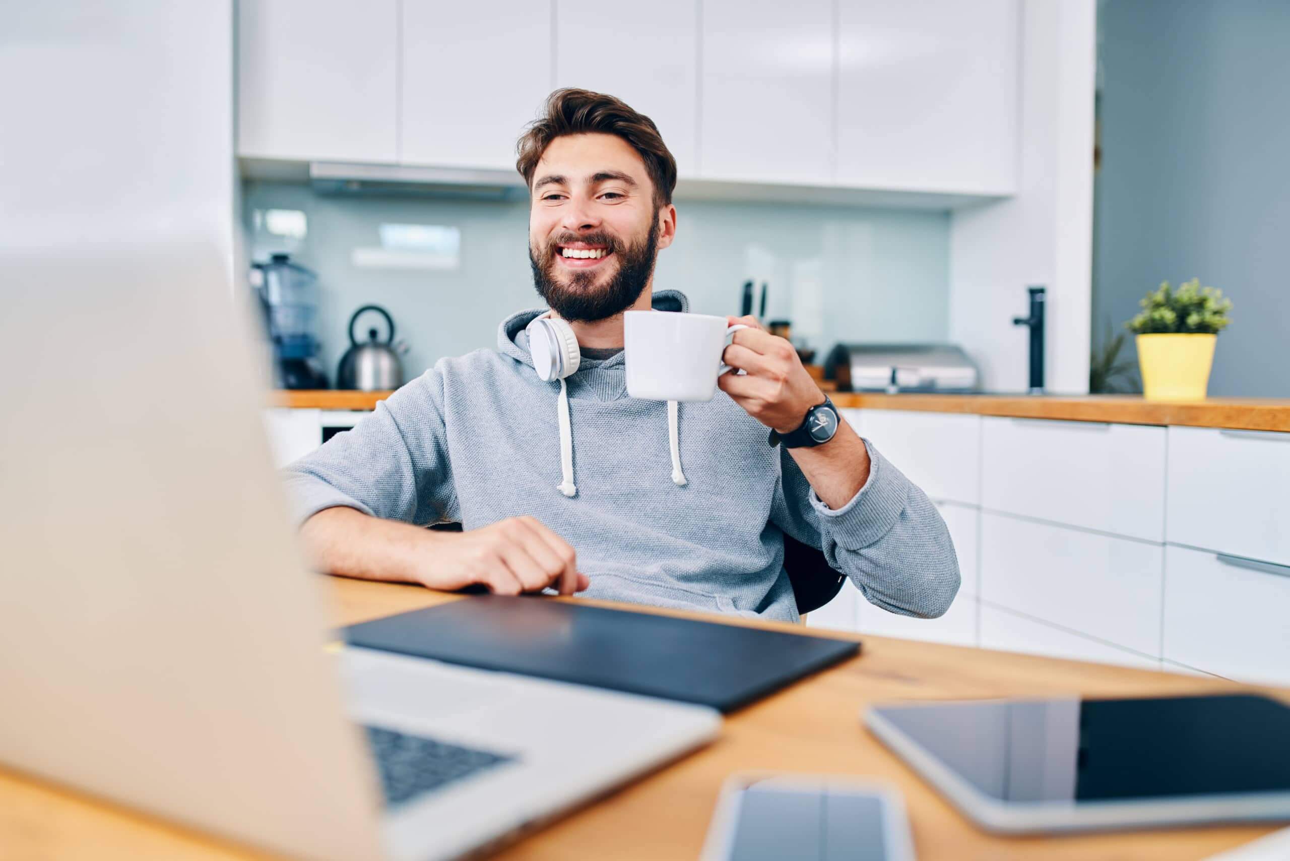 Joyful young web developer drinking coffee while taking break from work in home office